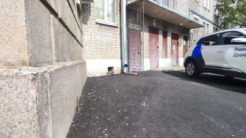 Легковой автомобиль на свежем асфальте во дворе у кирпичного дома с водосточной трубой и зелёными насаждениями