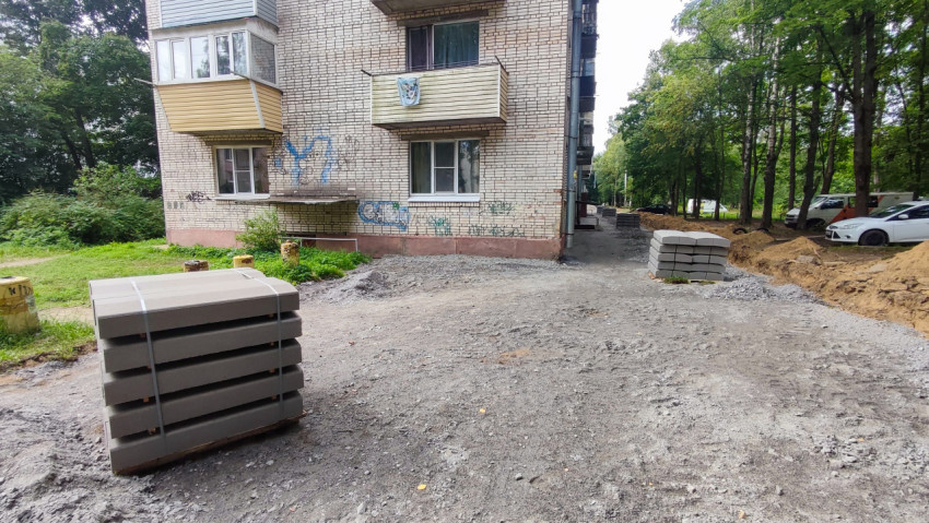 Паллеты с тротуарной плиткой и щебёночное основание у фасада жилого дома во время благоустройства двора