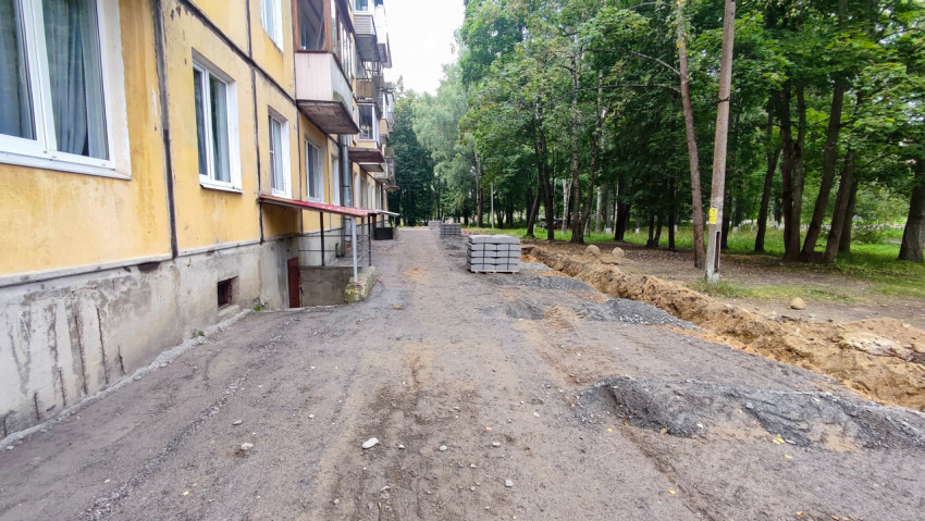 Разрытая траншея и склад плитки вдоль жилого дома при ремонте дворового проезда