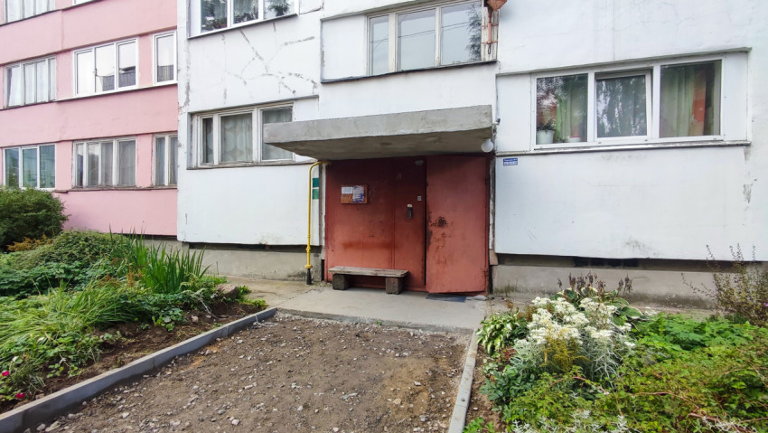 Вход в подъезд жилого дома с бетонным козырьком и лавкой рядом с ремонтом тротуара