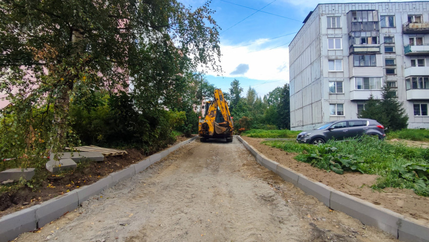 Экскаватор-погрузчик на новой дворовой дороге между домами с установленными бордюрами