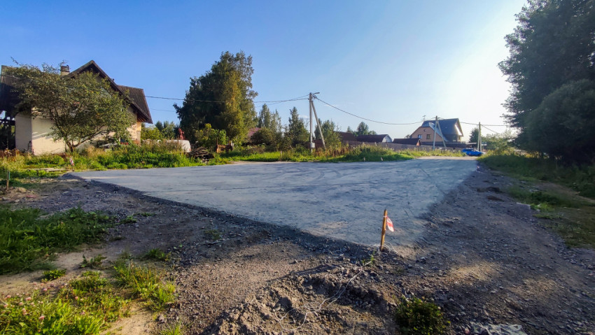 Широкий участок дороги с гладким покрытием и сигнальным колышком у частных домов