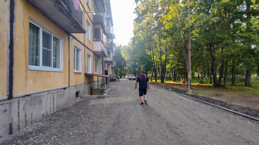 Мужчина идёт по грунтовому дворовому проезду вдоль жилого дома и аллеи деревьев