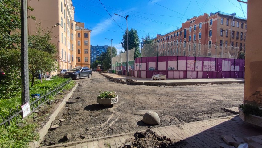 Ограждение спортивной площадки и двор с гравийным проездом среди городских домов