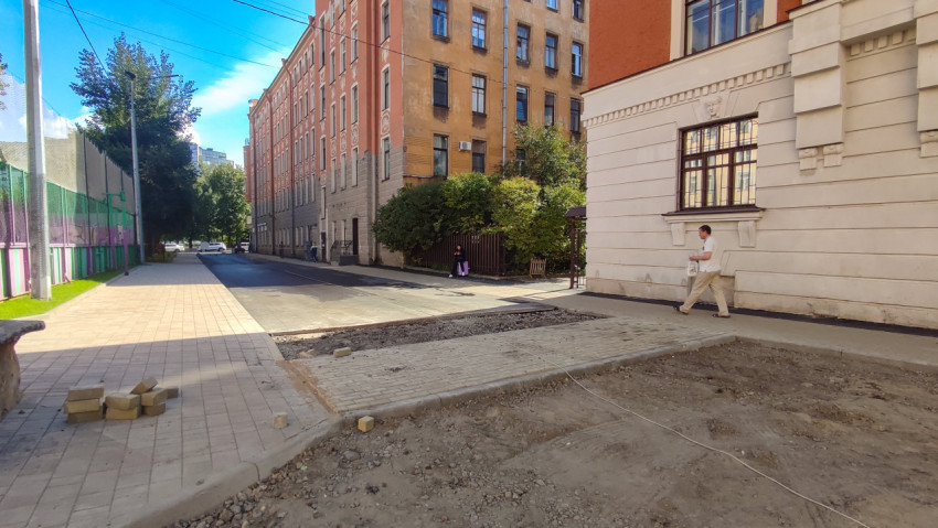 Пешеход идёт вдоль ограждения спортивной площадки и фасада со штукатурным декором