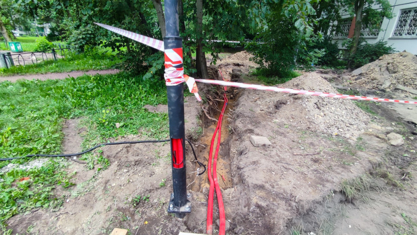 Траншея у тротуара с проложенными кабелями и сигнальной лентой
