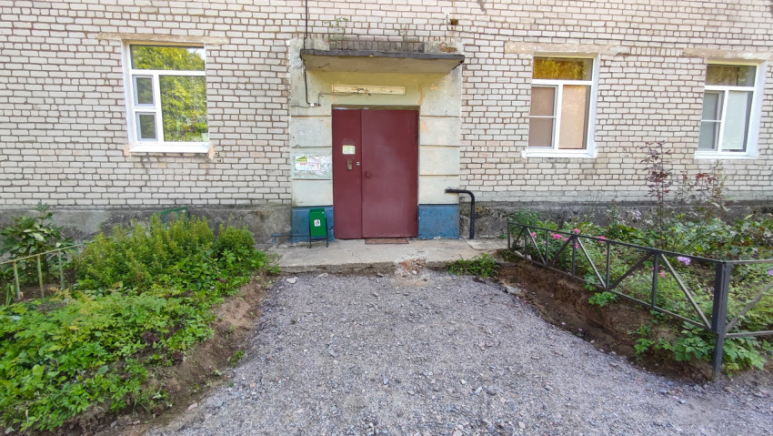 Вход в подъезд с красной дверью и разрытым покрытием у крыльца