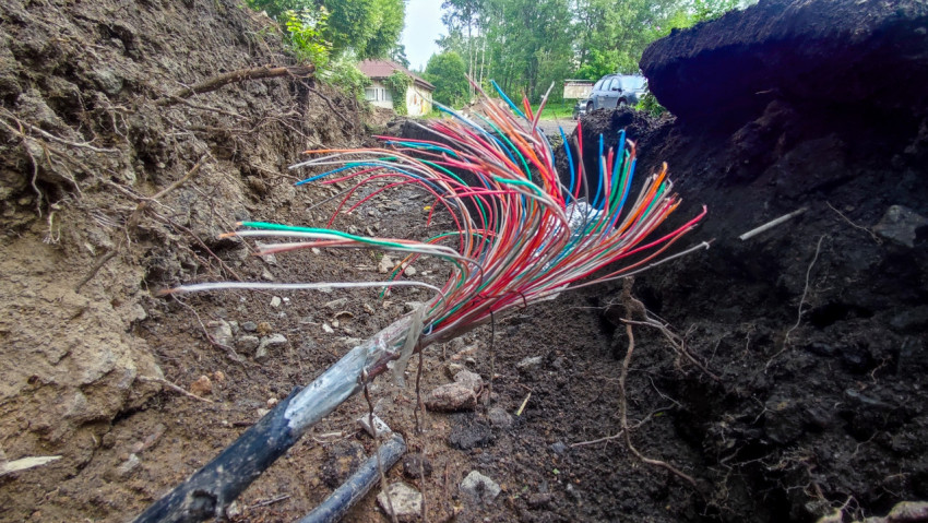 Разорванный многожильный кабель с цветными жилами в открытой траншее у дороги