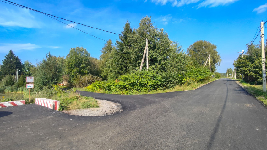 Свежий асфальт у развилки, рядом знаки и временные дорожные барьеры