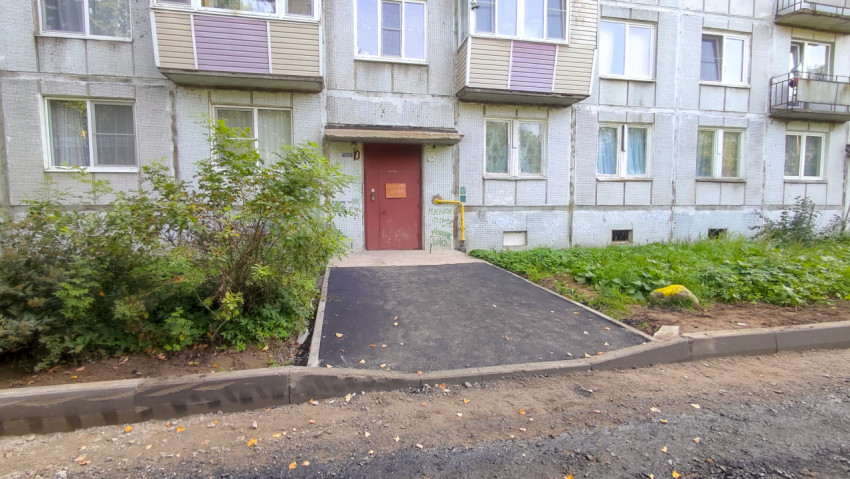 Вход в панельный дом с новой площадкой из асфальта и бордюрами у стены