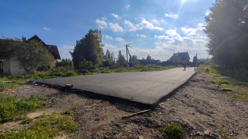 Свежий асфальт и обочина на сельской дороге с рабочим в жилете