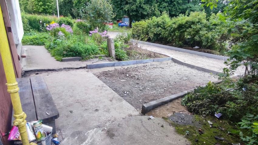 Ремонтируемая дворовая площадка с бордюрами у фасада дома, скамейкой и коммуникациями