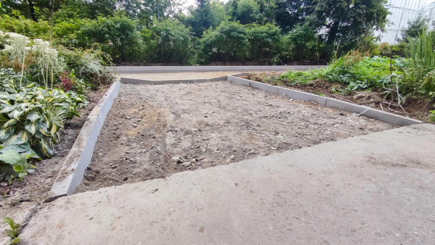 Установленные бордюры и щебёночное основание вдоль дворовой дорожки рядом с клумбой