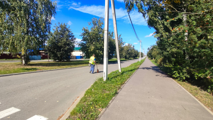 Работник измеряет участок дороги колесом рядом с тротуаром и линией опор