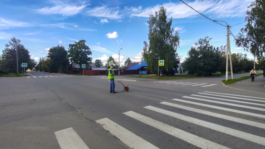 Широкая «зебра» на перекрёстке, рядом специалист с измерительным колесом и проезжающий велосипедист