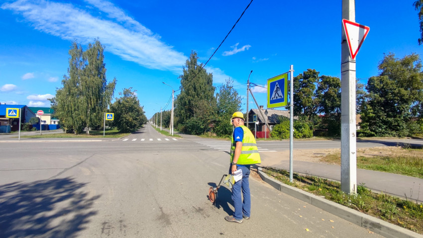 Работник в каске и жилете стоит у «зебры» с измерительным колесом и бумагами