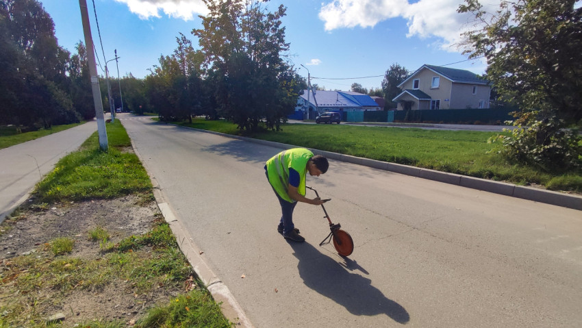 Дорожник наклоняется к измерительному колесу и фиксирует точку на асфальте