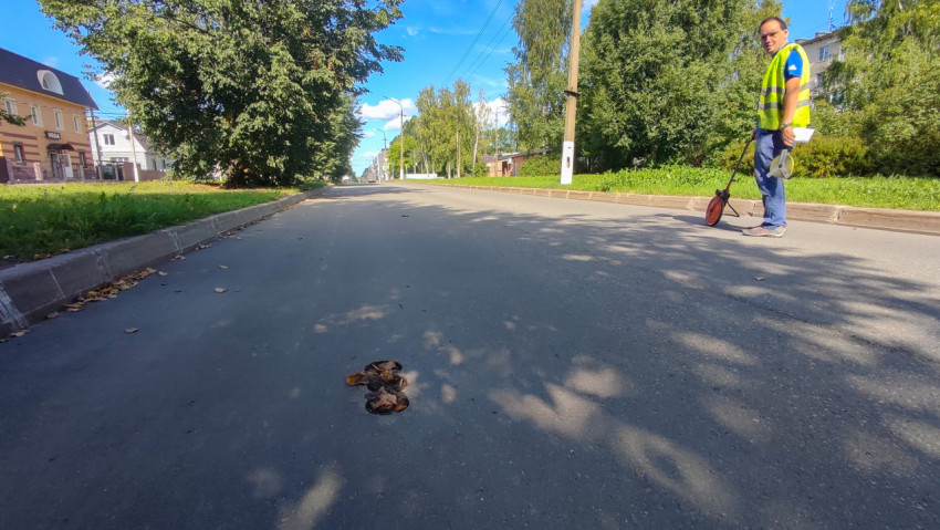 Инженер с мерным колесом осматривает яму в асфальте и делает замеры