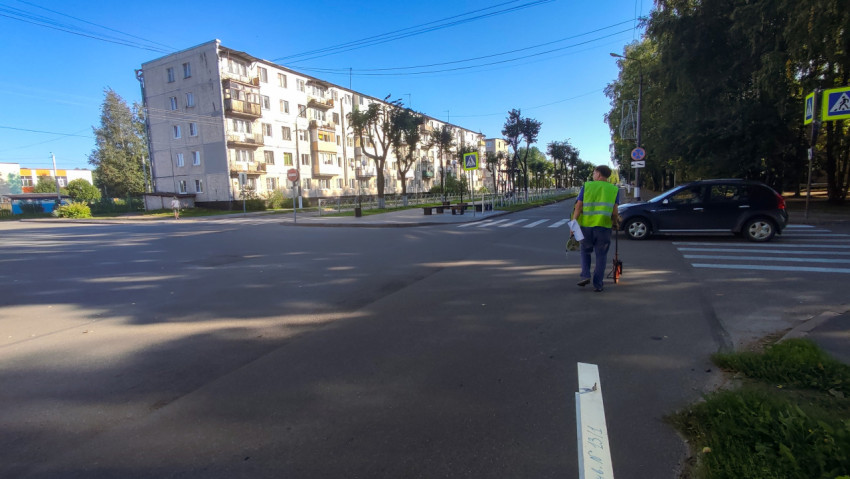 Мужчина с мерным колесом идёт через перекрёсток по разметке пешеходного перехода