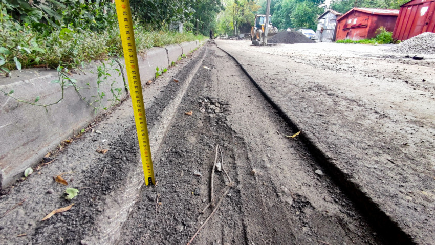 Замер глубины фрезерованного слоя у бордюра складной рулеткой на участке дорожного ремонта