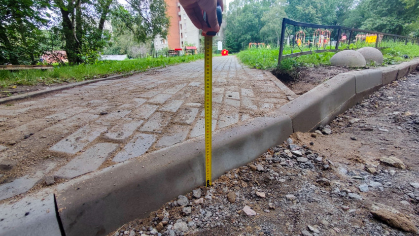 Рулетка у бордюра рядом с тротуарной плиткой при проверке отметки покрытия