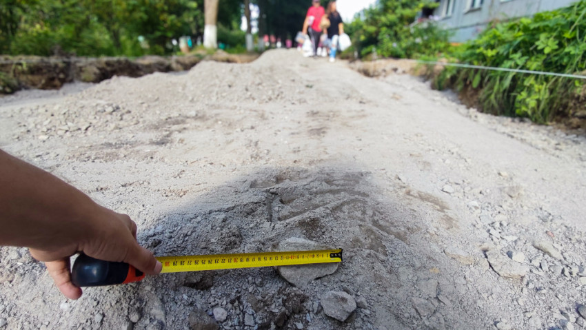 Рука удерживает рулетку при замере камня на щебёночном основании ремонтируемого дворового проезда