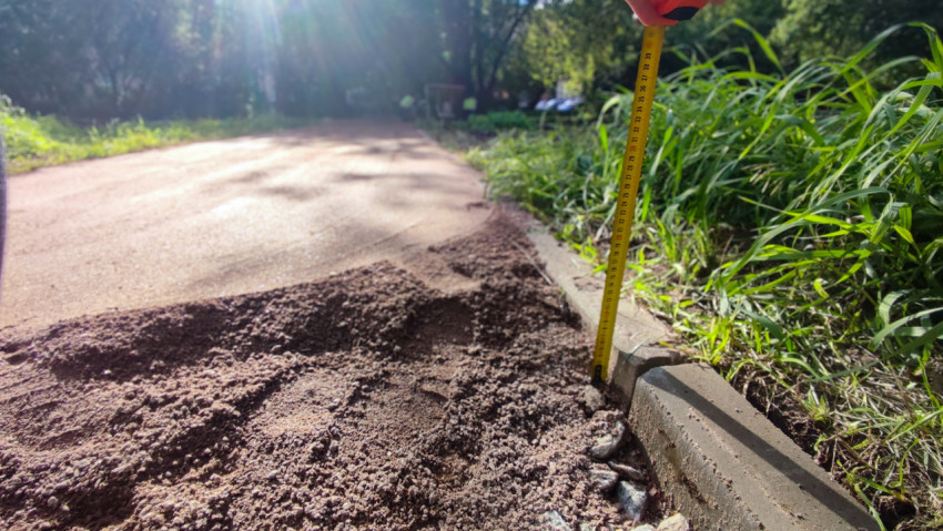 Измерение глубины песчаной подсыпки у бордюра на краю асфальтовой дороги
