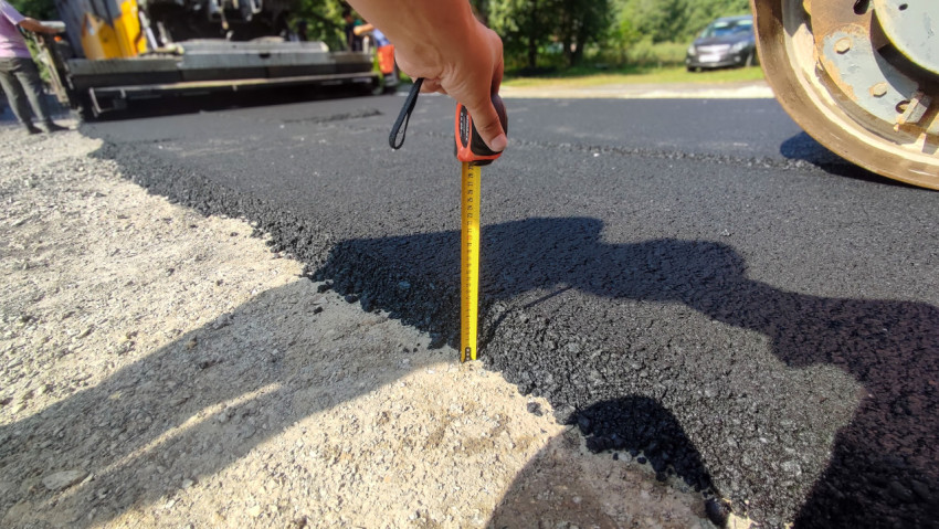 Рулеткой измеряют толщину свежего асфальта у кромки покрытия рядом с катком