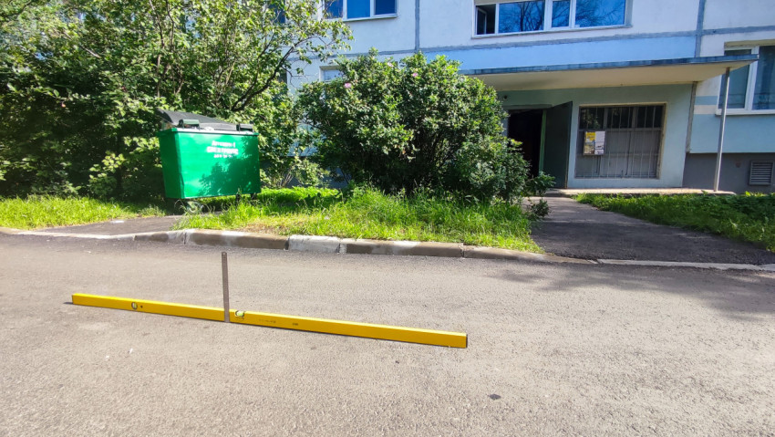 Длинный строительный уровень на асфальте у тротуара при проверке ровности дворового проезда