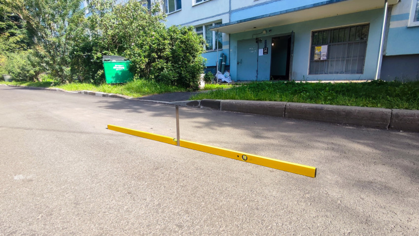 Измерение ровности асфальта уровнем и рейкой у подъезда жилого дома во дворе