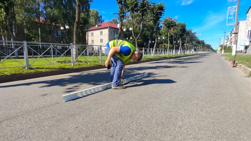 Инженер с телефоном фиксирует замер ровности асфальта рейкой прямо на улице