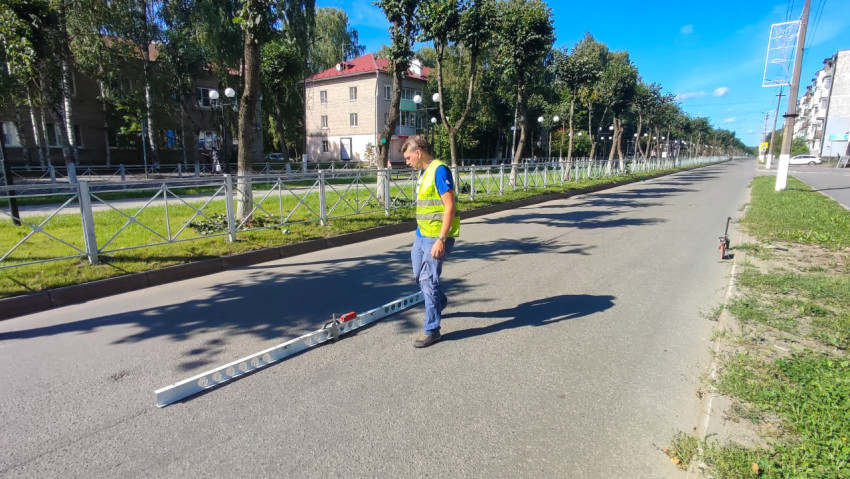 Рабочий стоит у измерительной рейки на пустой полосе и готовит замер ровности