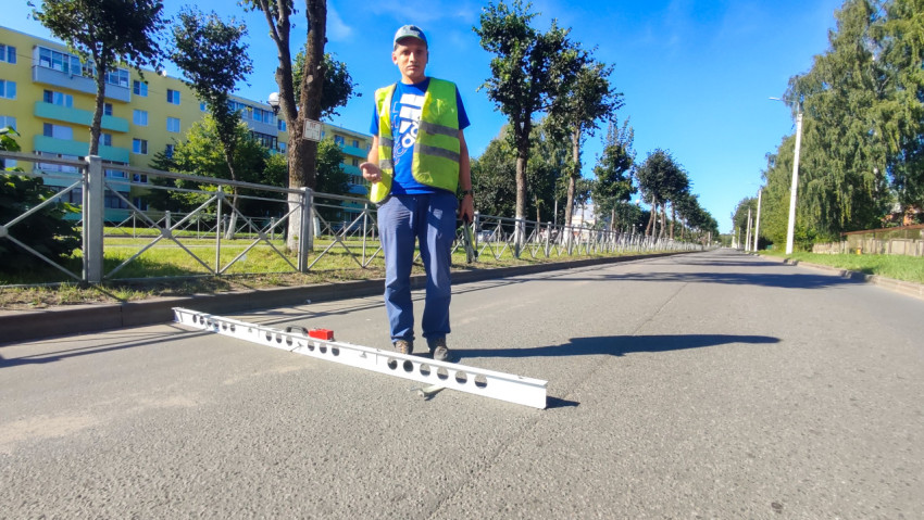 Инженер с измерительной рейкой стоит на улице и готовится замерять неровности дорожного покрытия