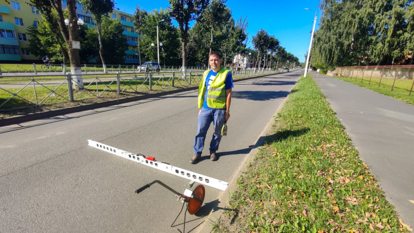 Рабочий проверяет дорожное покрытие рейкой и измерительным колесом на улице