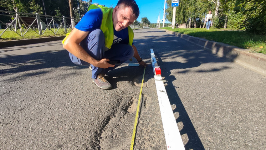 Рулеткой и рейкой измеряют размеры выбоины на городском асфальте