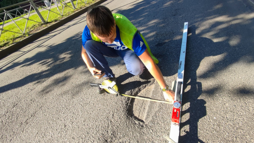 Сверху видно, как рулеткой меряют дефект асфальта рядом с рейкой для контроля