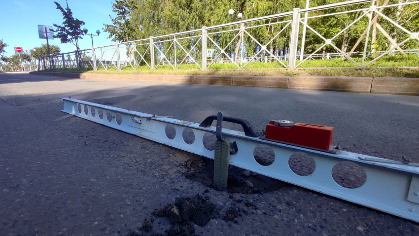 Крупный план: рейка лежит на асфальте, а клин показывает глубину выбоины