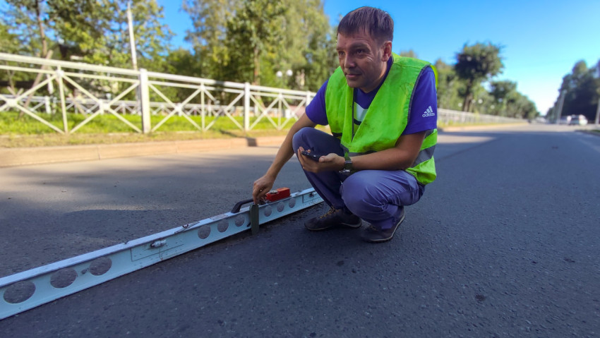 Инспектор в сигнальном жилете проверяет ровность асфальта рейкой и измерительным клином