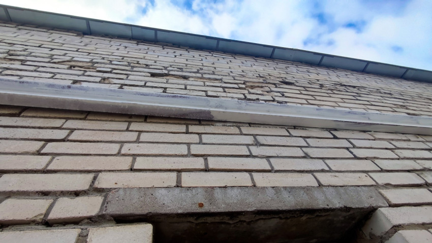 Металлический карниз и стык с кирпичной кладкой на фасаде здания в пасмурную погоду