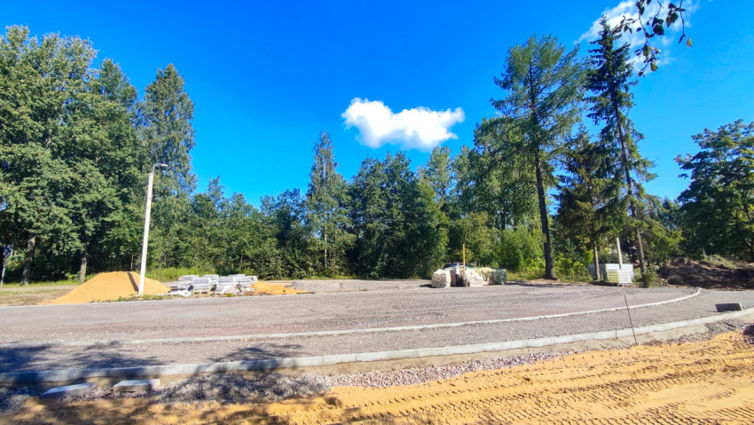 Площадка дорожных работ с кучами песка и уложенными бордюрами у леса