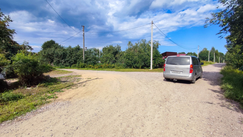 Грунтовая дорога на перекрёстке в посёлке с легковым автомобилем и линиями электропередачи