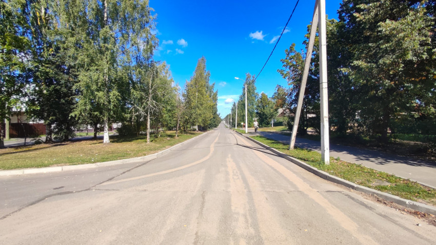Длинная прямая дорога с тротуарами, фонарями и песком на асфальте после уборки