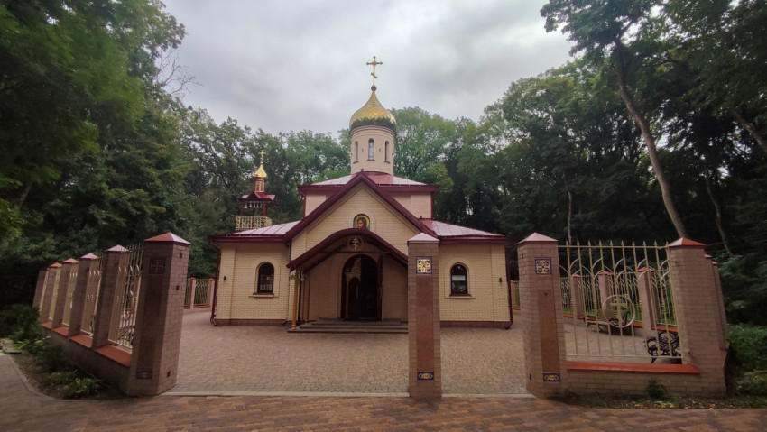 Фасад православного храма с куполом и симметричной оградой у лесной аллеи