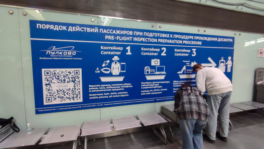 Стенд Пулково с QR-кодом и зона сборки вещей после досмотра