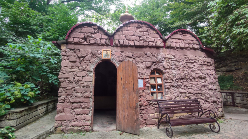 Каменная часовня с открытой дверью и лавкой на площадке в лесу