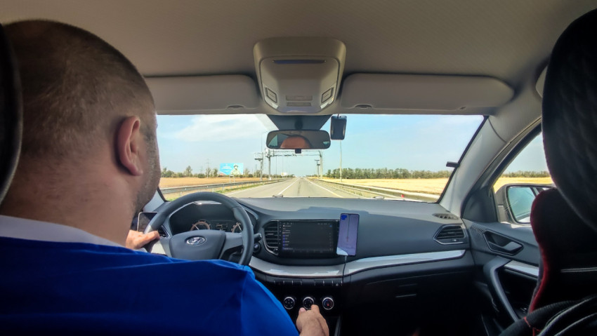 Салон автомобиля на трассе: водитель, приборная панель и навигация на смартфоне