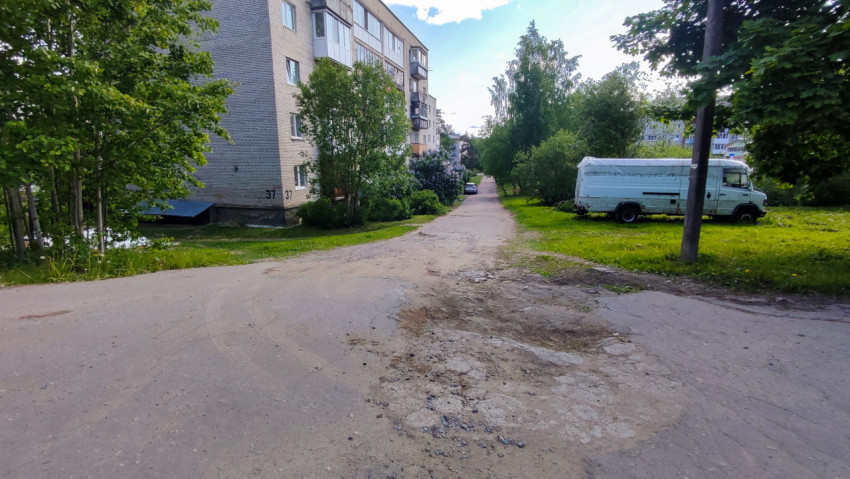 Дворовая дорога у жилого дома с поврежденным асфальтом