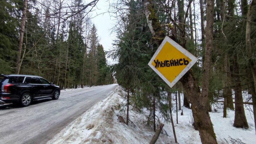 Автомобиль на зимней дороге и знак «Улыбнись» в лесу