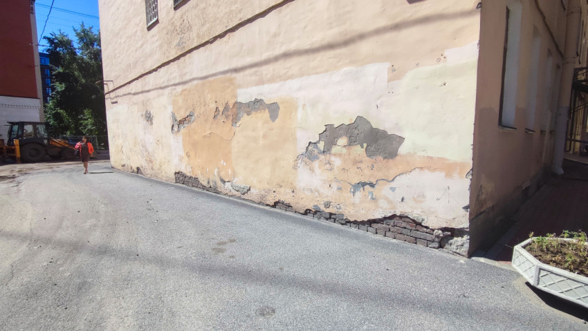 Облупившийся фасад здания с оголённой кирпичной кладкой у основания