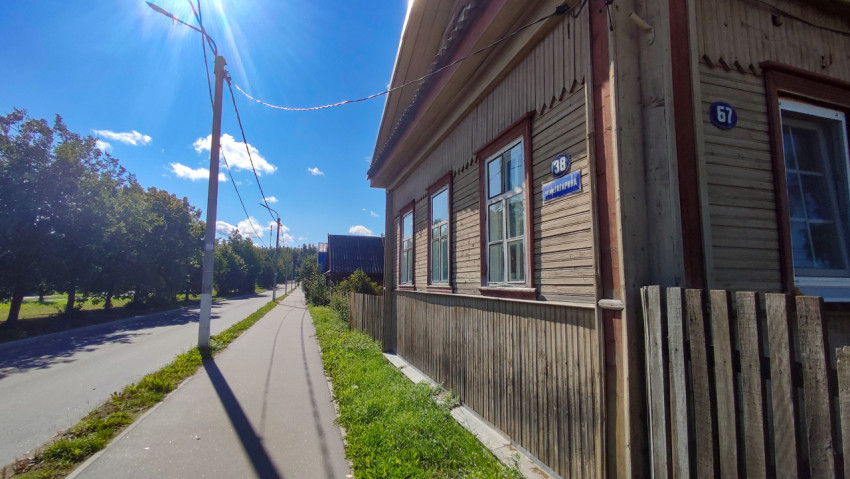 Крупный план фасада деревянного дома с адресной табличкой и уличными указателями на солнечном свету